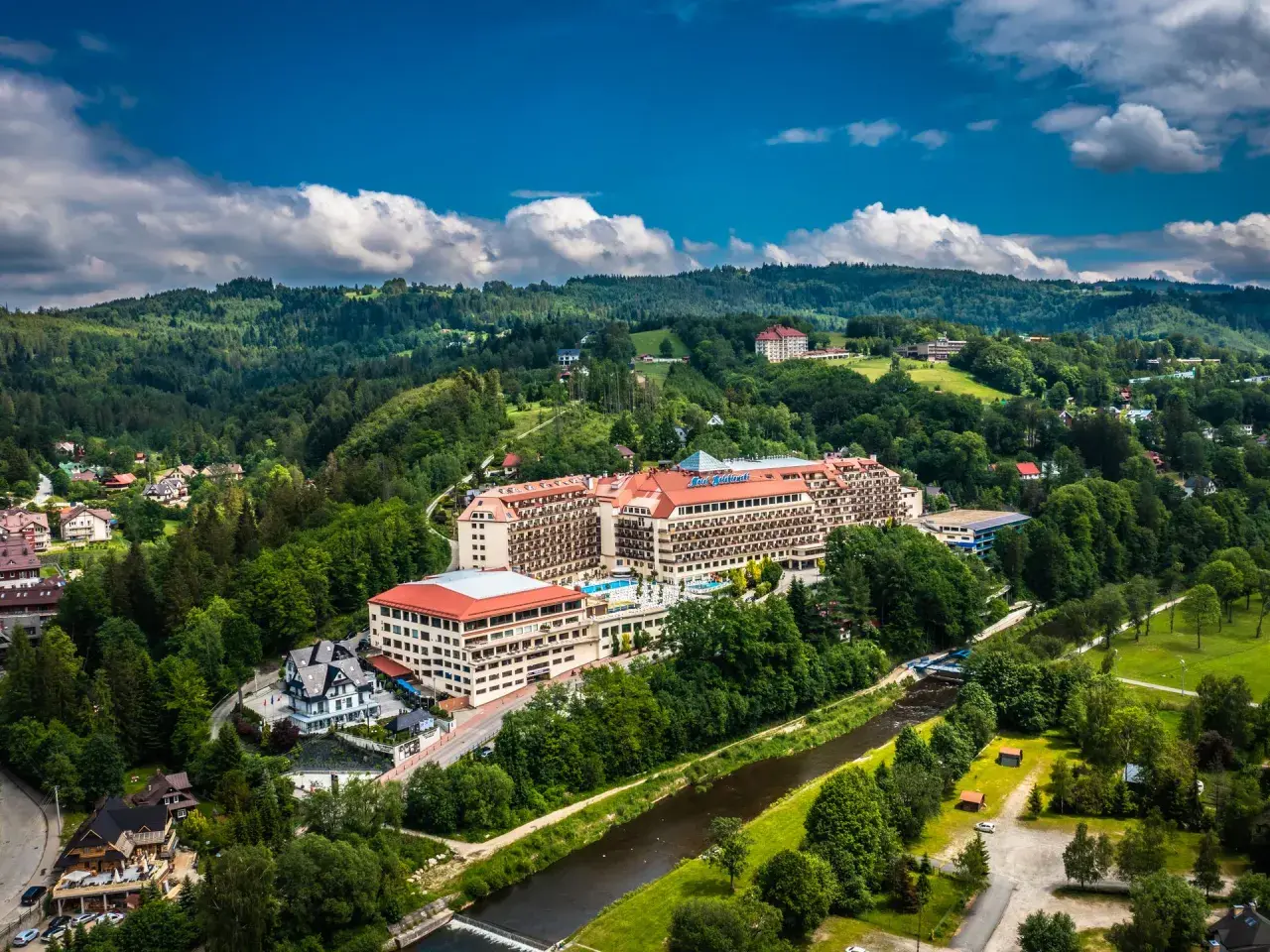 Gdzie są hotele Gołębiewski? Rozległy kompleks hotelowy w otoczeniu zielonych wzgórz i rzeki.